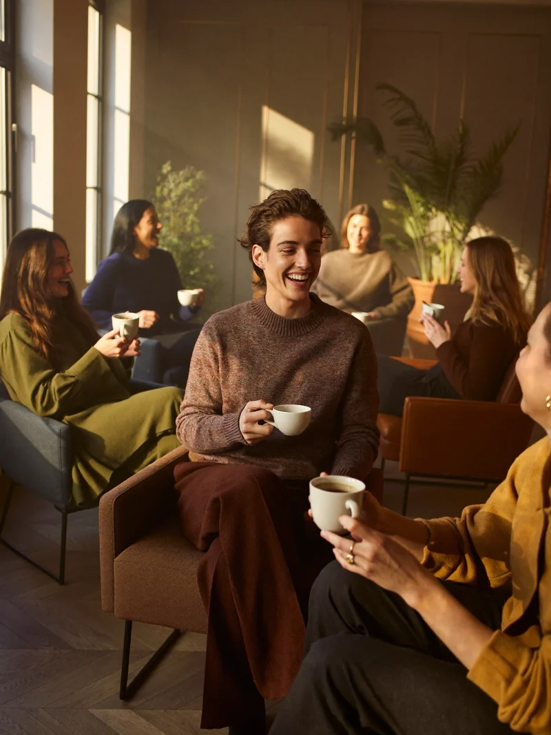 Illustration: sechs Personen in Sesseln einer warmen Lounge im Gespraech bei Kaffee